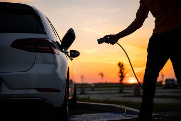 Silhouette of man inserting plug into the electric car charging socket Silhouette of african american man plugging an EV plug into his car for charging at station electric car stock pictures, royalty-free photos & images